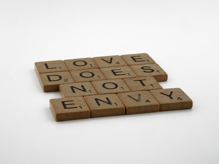 Inspirational quote 'Love Does Not Envy' spelled with Scrabble tiles on white background.