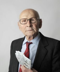An elderly man with glasses holding dollar bills, representing wealth and financial security.