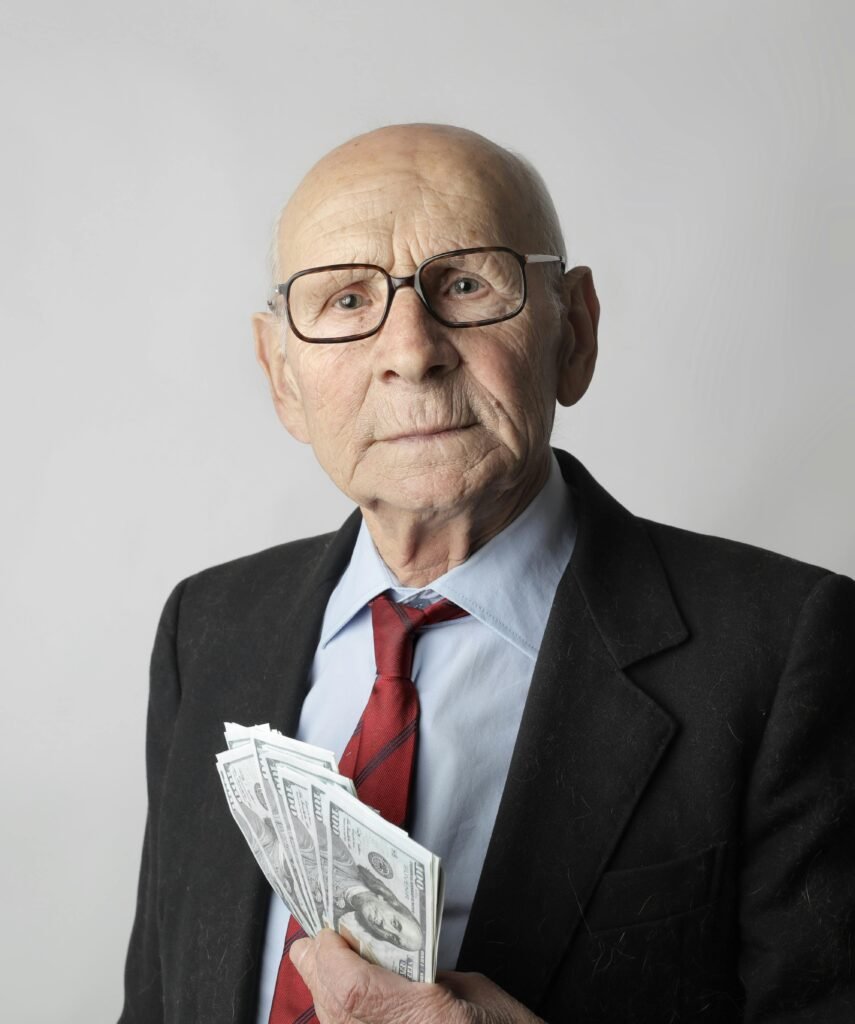 An elderly man with glasses holding dollar bills, representing wealth and financial security.