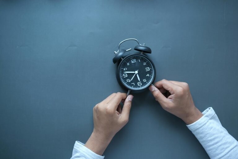 Hands adjusting a classic black alarm clock on a blue background with ample copy space.